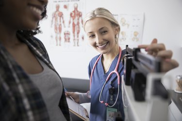 Smiling female nurse checking weight of woman on scale in clinic examination room