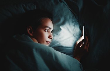 Close-Up Of Woman Using Phone While Lying On Bed In Darkroom