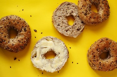 Closeup of a 12 grain bagel with butter on a yellow background