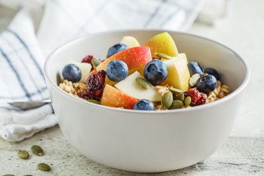 Bircher muesli or overnight oatmeal with apple, banana and blueberries in gray bowl.