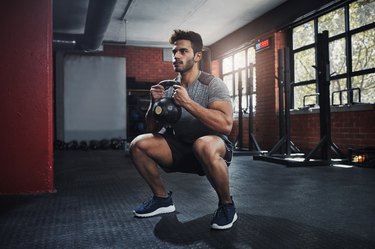 Man doing squats with a kettlebell in the gym