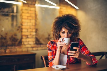 Young woman at cafe drinking coffee and using mobile phone