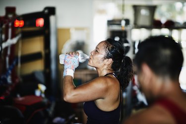 Sweating female boxer drinking water after workout in boxing gym