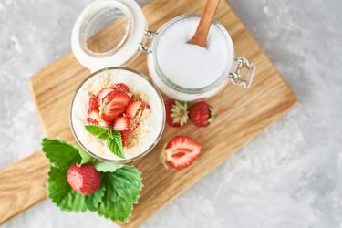 granola or yogurt with strawberry in glass, fresh berries and jar with sugar on a cutting board, top view