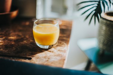 Single Glass of Fresh Orange Juice on wooden table with palm on the side
