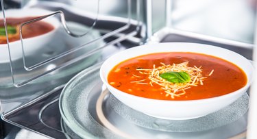 Inside view of new clean staniless microwave oven with a tomato soup in white plate