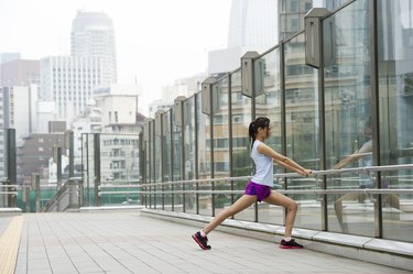 Person wearing a white T-shirt and purple shorts stretching their calves outside.