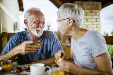 A happy senior couple talking while eating breakfast on a balcony.