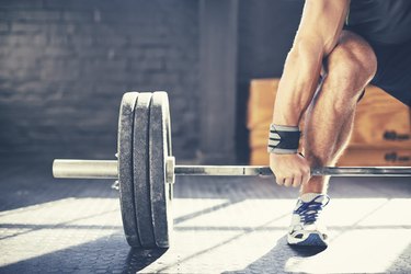 man deadlifting heavy barbell in gym, which could lead to hemorrhoids