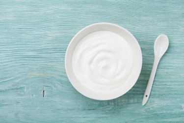 Fresh greek yogurt in bowl on rustic wooden table top view.