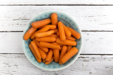 Baby carrots in bowl on white wood