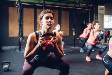 Women training in gym, squatting and lifting kettle bells