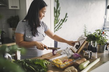 a person using a tablet in their kitchen and cutting vegetables to meal prep a healthy meal as part of a self-care practice