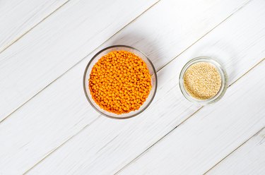 Glass plates with red lentils, sesame seeds and a large glass plate stand on wooden table