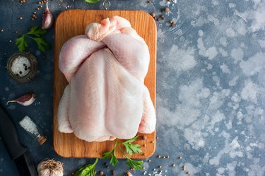 Whole raw chicken on a wooden board with spices for cooking, top view, horizontal, copy space