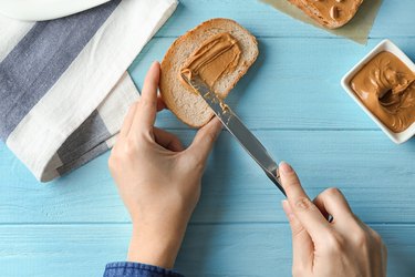 Woman spreading peanut butter on toast over table