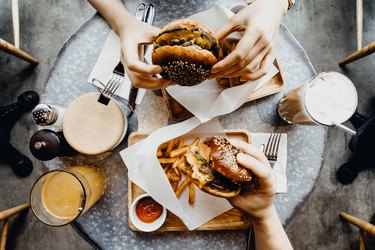 Top view of friends having a good time eating burgers with french fries and drinks in a cafe