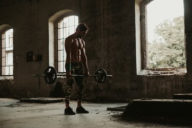 Athletic man holding weights in deadlift in an old building