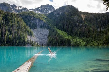 A girl practicing swimming safety dives into the blue waters of Joffre Lakes with mountain background