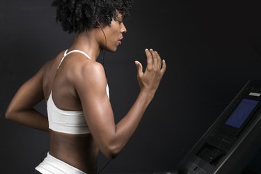 Side view of woman running on treadmill while listening music against wall in gym