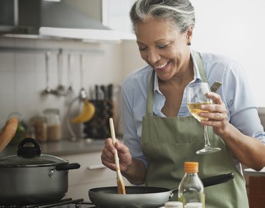 Hispanic woman cooking with wine in kitchen