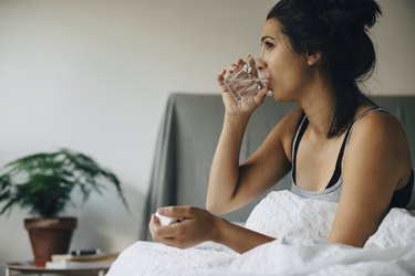 Person taking medicine while sitting on bed at home, to avoid waking up bloated
