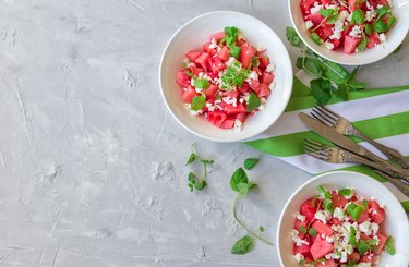 Fresh organic salad with watermelon, feta cheese and mint in bowls on light gray concrete background.