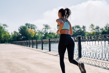 Back view of fit woman running outdoors by river