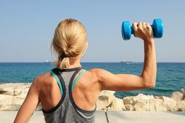 Young athletic woman exercising outdoors: overhead press for upper body strength