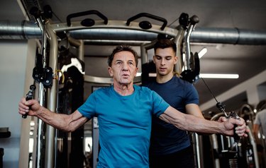 A man with a young trainer doing strength workout exercise in gym.