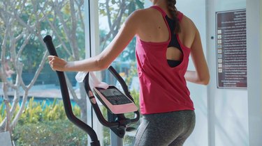 Sporty young woman exercising on elliptical machine at the condo gym