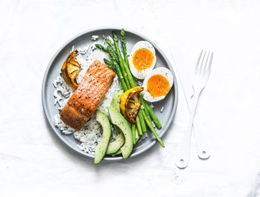 Healthy delicious balanced lunch - baked salmon, rice, asparagus, avocado and boiled egg on a light background, top view