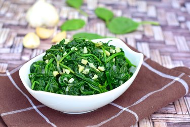 Healthy sautéed magnesium-rich spinach with minced garlic in white bowl on kitchen cloth