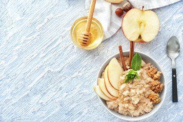 Tasty oatmeal with apple and walnut in bowl on table