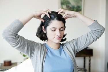 A woman with short brown hair performing a scalp exercise at home