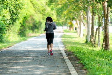 Healthy woman jogging run and workout on road outdoor. Asian runner people exercise gym with fitness session, nature park background. Healthy and Lifestyle Concept.