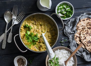 Indian dhal in  cooking pan with jasmine rice, coriander and whole grain flatbread on dark background, top view. Flat lay. Healthy vegetarian food