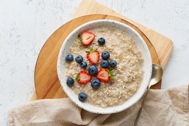 Oatmeal porridge rustic with berries, dash diet, on white wooden background top view