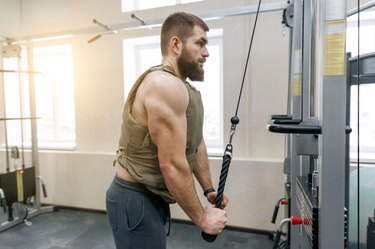Muscular caucasian bearded man doing exercises dressed in weighted vest in the gym, military style