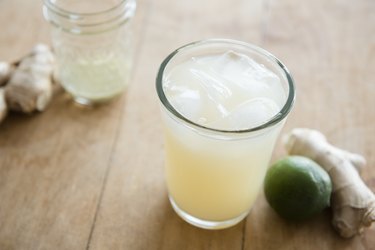 Schweppes ginger ale with ice cubes in drinking glass on wooden table is not good for stomach flu in 15-month-old