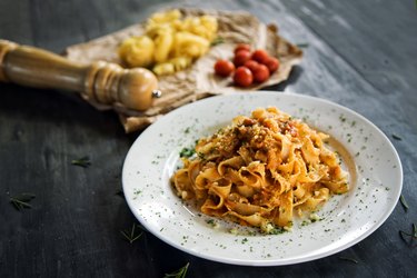 Homemade pasta on white dish with tomatoes and dough in background
