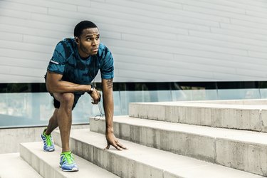 Young male runner warming up on city steps