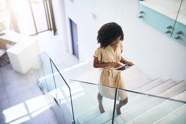 A professional woman walking up the stairs in her office building while working on a tablet