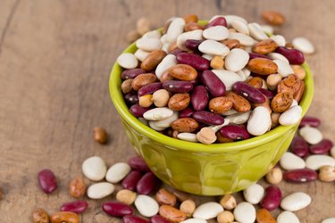 various beans in green bowl on wooden surface