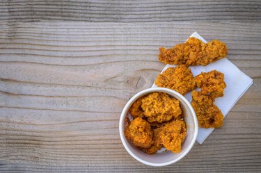 Fried chicken in a white bowl and on napkins on a wooden table.