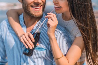 Close up shot of handsome young guy piggybacking his girlfriend drinking soft drink outdoors.