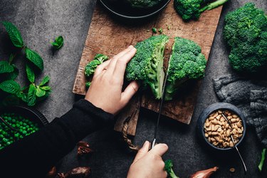 Woman cutting fresh broccoli on cutting board, dark background