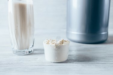 Scoop with dry protein powder, container and glass of drink