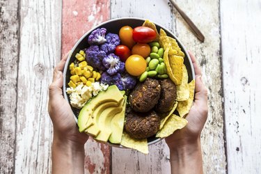 Girls hands holding Quinoa veggie bowl of vegetables, feta, nachos and quinoa fritters