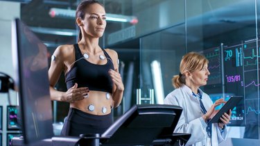 A person runs on a treadmill while a scientists measures their cardio exercise heart rate